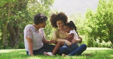 Çoklu nesil melez aile bahçede eğleniyor, çimenlerde oturuyor, sarılıyor, birbirlerine bakıyor ve gülümsüyor, ağır çekimde.