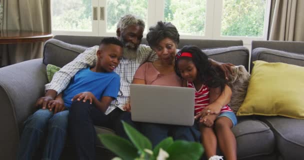 上了年纪的混血种族夫妇在家里度过了一段愉快的时光 他们和孙子孙女坐在沙发上 用笔记本电脑 社交场合的疏远和自我隔离 在考伦威病毒肆虐的时候 他们慢吞吞地把自己关在隔离室里 — 图库视频影像