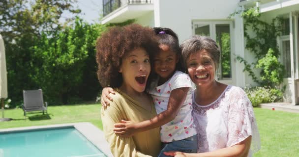 多代混血种族的家庭在一个有游泳池的花园里享受时光 他们站在游泳池边 抱着镜头 慢吞吞地微笑着 — 图库视频影像
