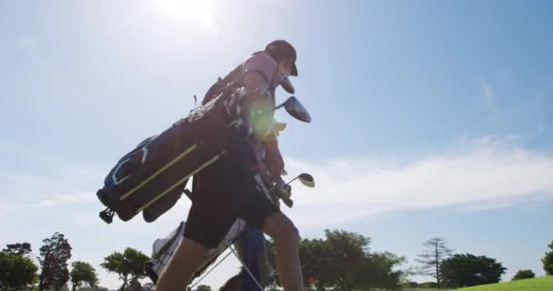 在阳光灿烂的日子里 两名白人男性高尔夫球手头戴高尔夫球帽 身穿高尔夫球衣 拿着高尔夫球杆 提着高尔夫球袋 在阳光的映衬下 慢吞吞地微笑着 谈着话 他们的视角很低 — 图库视频影像