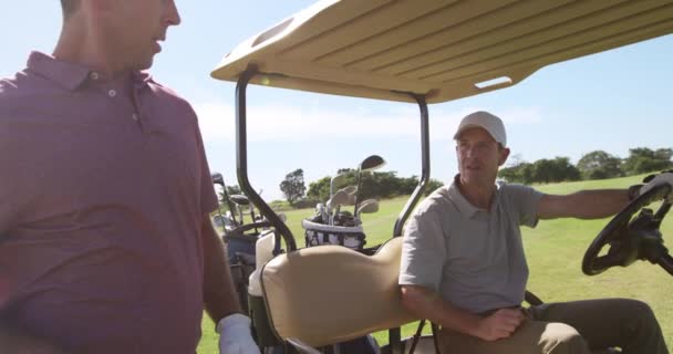天气晴朗的日子里 两名白人男子高尔夫球手头戴球帽 身穿高尔夫球衣 在高尔夫球场上玩耍 爬上一辆高尔夫球车 准备慢吞吞地穿过球场 — 图库视频影像