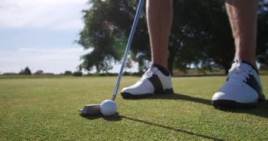 Alçak kesim, güneşli bir günde golf sahasında şort giyen beyaz bir erkek golfçünün bacaklarının yan görüntüsü. Elinde golf sopasıyla topu yavaşça son deliğe doğru atıyor.