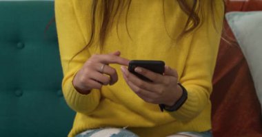 Kafkasyalı bir kadının evinin ortalarına yakın, karantina odasında sosyal mesafeler ve izolasyon, oturma odasındaki bir kanepede oturması, akıllı telefon kullanması.