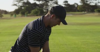 Güneşli bir günde, golf sahasında şapkalı ve golf kıyafetli, golf sopası sallayan ve topa yavaş çekimde vuran beyaz bir erkek golfçüye yaklaş.