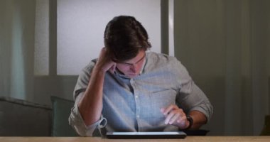 Beyaz bir adam evde vakit geçiriyor, sosyal uzaklık ve tecrit karantinada, masada oturuyor, tablet kullanıyor.