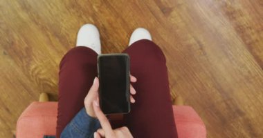 Kafkasyalı bir kadının evde vakit geçirmesini, sosyal mesafeyi ve karantinada kendini tecrit etmesini oturma odasında bir koltukta oturmasını, akıllı telefon kullanmasını tepeden izlemek.