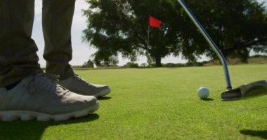 Güneşli bir günde elinde golf sopasıyla golf sahasındaki erkek golfçünün bacakları, kırmızı bayrakla işaretlenmiş son deliğe doğru yükseliyor.