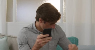 Beyaz bir adam evde vakit geçiriyor, sosyal uzaklık ve tecrit karantinada, oturma odasındaki bir kanepede oturuyor, akıllı telefon kullanıyor, kredi kartını tutuyor.