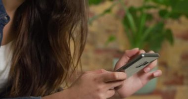 Kafkasyalı bir kadının evinin ortalarına yakın, karantina odasında sosyal mesafeler ve izolasyon, oturma odasındaki bir kanepede oturması, akıllı telefon kullanması.