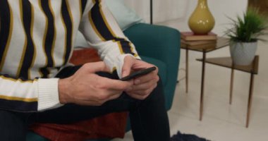 Kafkasyalı bir adamın evinin ortalarına yakın, karantina odasında sosyal mesafeler ve kendini izole etme, oturma odasında bir kanepede oturması, akıllı telefon kullanması.