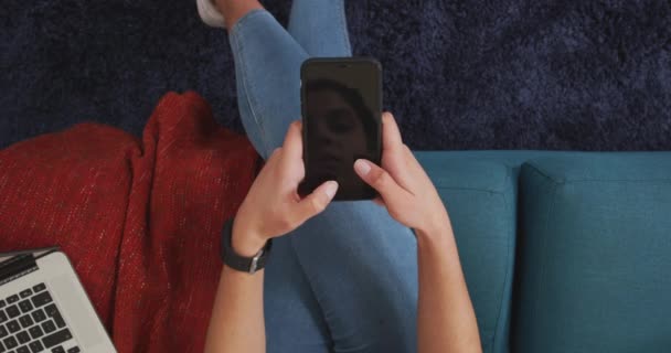 自宅で時間を過ごす白人女性のオーバーヘッドビュー 隔離されたロックダウンでの社会的距離と自己隔離 彼女のリビングルームのソファに座って スマートフォンを使用して — ストック動画