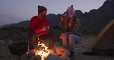 Kafkasyalı çift dağlara seyahatlerinde iyi vakit geçiriyorlar, akşamları kamp ateşinin yanında oturuyorlar, sıcak kıyafetler giyiyorlar, kahve içiyorlar, yavaş çekimde.