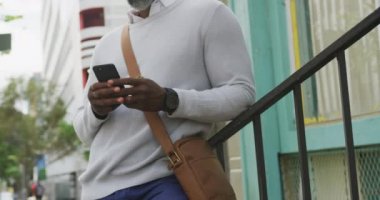 Afrika kökenli Amerikalı bir adam gün boyunca şehir sokaklarında geziyor, tırabzanlara yaslanıyor ve akıllı telefonunu kullanıyor..