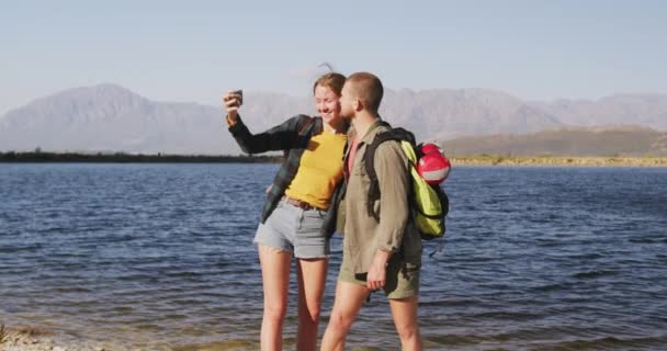 山への旅行で楽しい時間を過ごしている白人のカップル 海岸に立って 自撮りを取ります 遅い動きで晴れた日にキスと抱擁 — ストック動画