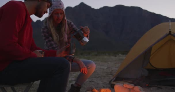 当天晚上 这对白种人夫妇穿着暖和的衣服 坐在篝火边 慢吞吞地把咖啡倒入一只金属杯子里 度过了一段愉快的登山之旅 — 图库视频影像