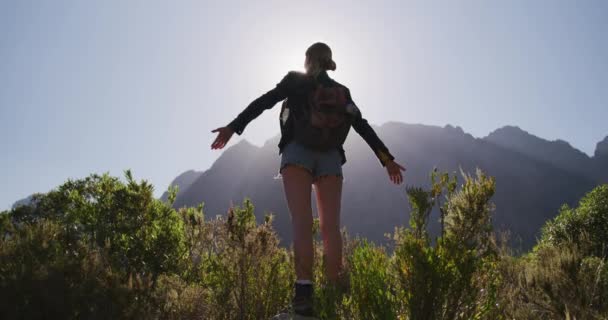 山への旅行で楽しい時間を過ごしている白人女性の後部ビュー 山の下のフィールドに立って ビューを楽しんで 彼女の腕を広く保持 スローモーションで晴れた日に — ストック動画