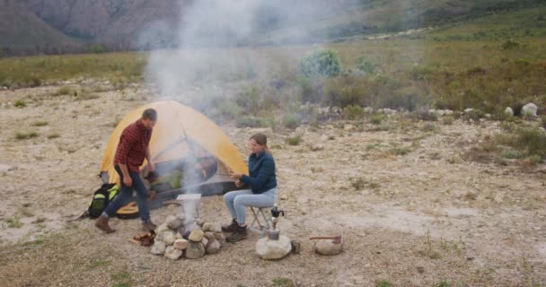 山への旅行で楽しい時間を過ごしている白人のカップル キャンプファイヤーに座って スティック上のソーセージを調理 スローモーションで — ストック動画