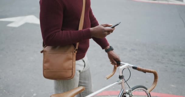 アフリカ系アメリカ人の男性が自転車を持ちスマートフォンを使って街中を歩き回っています — ストック動画