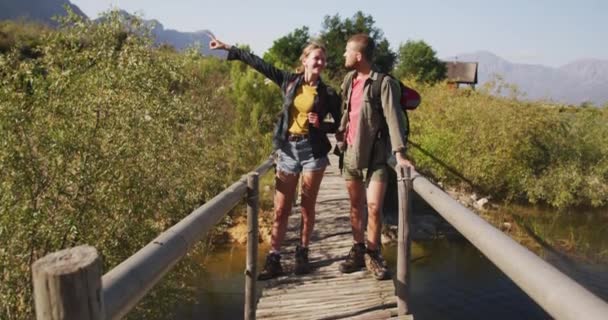 山への旅行で楽しい時間を過ごしている白人のカップル 橋の上に立って 晴れた日に景色を楽しみます スローモーションで — ストック動画