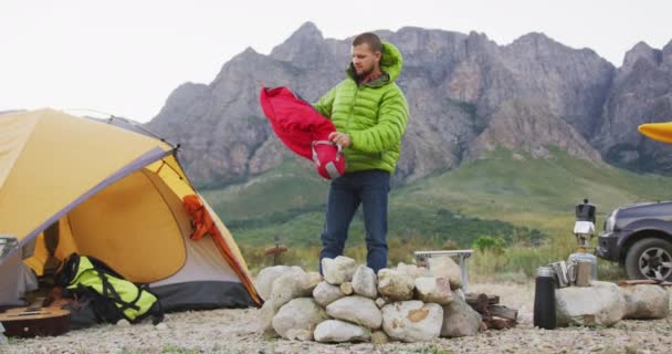 山への旅行で楽しい時間を過ごしている白人男性は テントのそばに立って ゆっくりとした動きの中で寝袋をアンパック — ストック動画