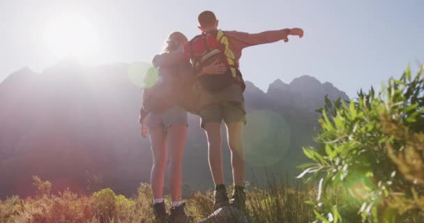 山への旅行で楽しい時間を過ごしている白人夫婦の後部ビュー 山の中で景色を楽しんでフィールドに立って 晴れた日に提起された腕で抱擁 スローモーションで — ストック動画