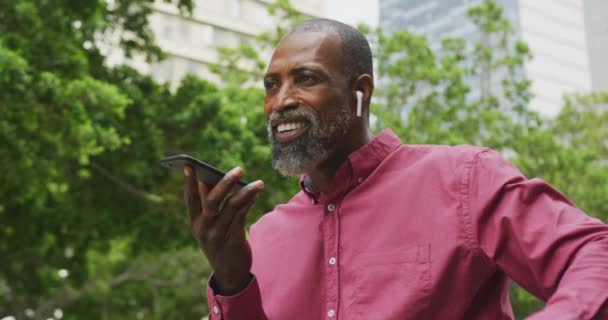 Афроамериканец Днем Ходит Улицам Города Носит Наушники Разговаривает Смартфону — стоковое видео