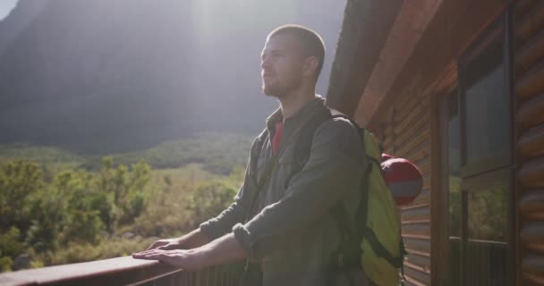 白种人喜欢爬山 站在小木屋的阳台上 在阳光灿烂的日子里慢吞吞地欣赏风景 — 图库视频影像