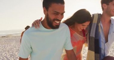 Gün batımında tropikal bir sahilde birlikte vakit geçiren, yürüyen ve gülümseyen melez ırk arkadaşlarının yan görüntüsü.