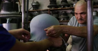 Yan görüntüde, karışık ırktan bir adam ve kıdemli bir melez adam bir şapka atölyesindeki bir teçhizatın ipini çekiştiriyorlar. Arka planda yavaş çekimde, yavaş çekimde makineler var.