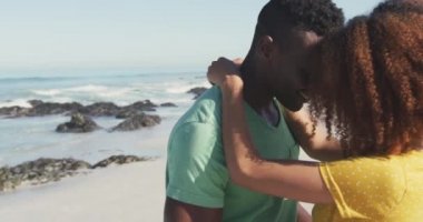 Afrika kökenli Amerikalı bir çiftin tropik bir plajda güneşlenirken, kucaklaşırken, dans ederken ve birbirlerine yavaşça bakarken yan görüntüsü.