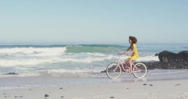 Afrika kökenli Amerikalı bir kadının tropikal bir plajda eğlenirken gülümsemesi ve bisiklete binerken ağır çekimde görüntüsü.