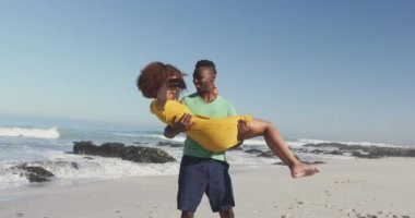 Afrika kökenli Amerikalı bir adamın tropik bir plajda güneşlenip, Afrika kökenli Amerikalı sevgilisini kucaklayıp, büyüttüğünü ve yavaş çekimde selfie çektiğini görmek.