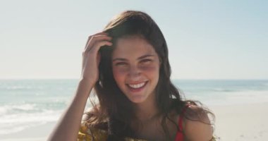 Kafkasyalı bir kadının, tropik bir plajda güneşin tadını çıkarırken, tararken, kameraya bakarken ve gülümserken ön görüntüsü.