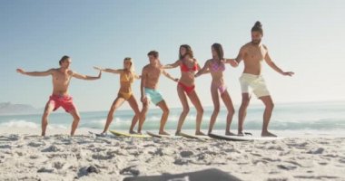 Çok ırklı bir arkadaş grubunun, tropikal bir plajda güneşin tadını çıkarması, gülümsemesi ve ağır çekimde sörf eğitimi alması ön planda.