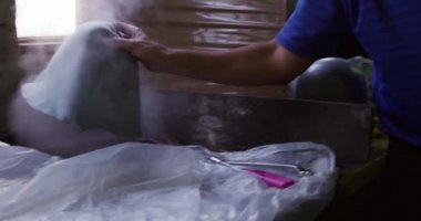 Bir şapka fabrikasındaki bir şapka atölyesinde çalışan son sınıf melez bir yarışçının arka planda ağır çekim ekipmanlarıyla yan görüntüsü.