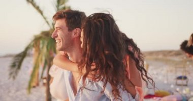Kafkasyalı bir çiftin gün batımında tropikal bir plajda eğlenirken yavaş çekimde gülümsemesi ve sırtına binmesi ön planda.
