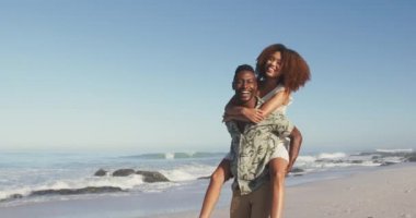 Afrika kökenli Amerikalı bir çiftin tropikal bir plajda güneşin tadını çıkarırken, yavaşça el ele tutuşurken, sırt üstü yatarken ve el kaldırırken.