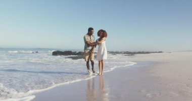 Afrika kökenli Amerikalı bir çiftin, tropikal bir plajda el ele tutuşarak, yürüyerek ve yavaşça dönerek güneşin tadını çıkarmasını izlemek.