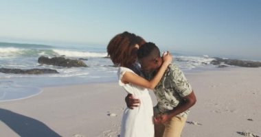 Afrika kökenli Amerikalı bir adamın tropikal bir plajda güneşlenip Afrika kökenli Amerikalı kız arkadaşını büyüttüğünü ve ağır çekimde gülümsediğini görüyoruz.