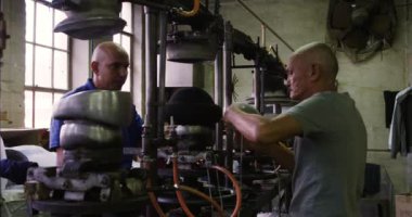 Melez bir ırk adamıyla kıdemli bir melez, arka planda ekipmanlarla birlikte bir şapka fabrikasının atölyesinde ekipman kullanıyor.