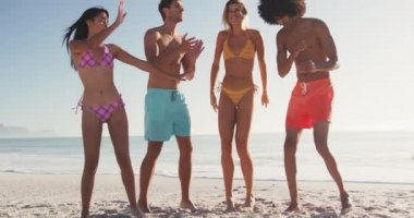 Tropik bir plajda güneşin tadını çıkaran, el kaldıran, dans eden, zıplayan ve gülen çok ırklı arkadaş grubunun ön görüntüsü.