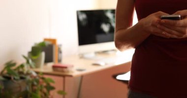 Beyaz kadın spor giysisi giyiyor, Coronavirus sırasında evde vakit geçiriyor, 19. hücrede, akıllı telefonunu, sosyal mesafesini ve kendini izole edişini kullanıyor..