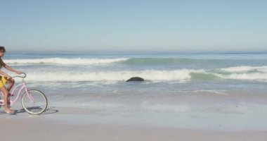 Afrika kökenli Amerikalı bir kadının tropikal bir plajda eğlenirken gülümsemesi ve bisiklete binerken ağır çekimde görüntüsü.