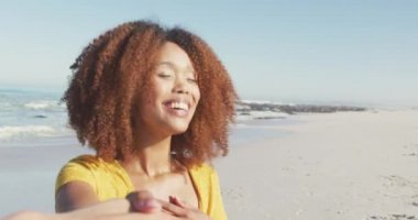 Afrika kökenli Amerikalı bir kadının tropikal bir plajda güneşin tadını çıkarırken erkek arkadaşının elini tutarken, yürürken ve gülümserken ağır çekimde.