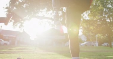 Düşük açılı, protez bacaklı, parkta çalışan, dizini göğsüne bastıran, kulaklıkla müzik dinleyen sakat bir ırk adamı.