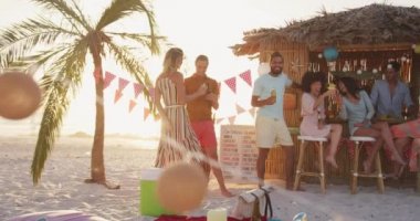 Gün batımında tropikal bir plajda eğlenen, yavaş çekimde konuşan ve gülümseyen melez ırk arkadaşlarının ön görüntüsü.