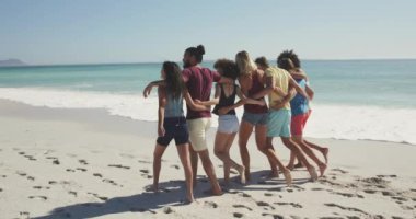 Çok ırklı bir arkadaş grubunun tropikal bir plajda güneşin tadını çıkarırken yavaş çekimde kucaklaşıp yürüdüğünü görmek.