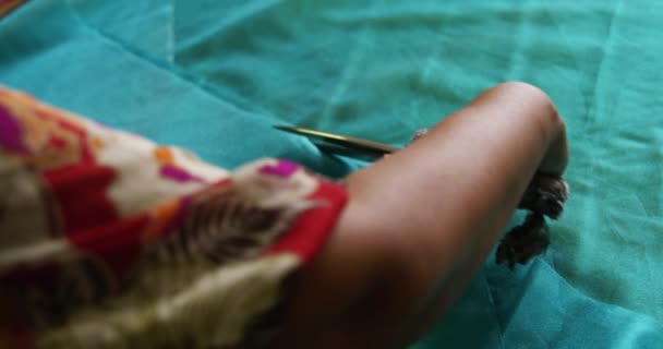 一位身穿围裙的混血儿站在一家帽厂的工作台上 用剪刀剪断了一块松软的蓝色材料 动作缓慢 — 图库视频影像