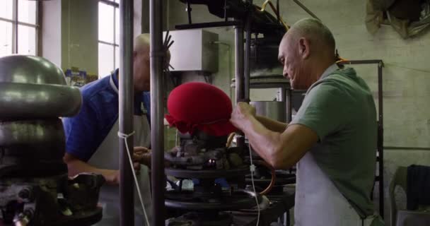 帽子工場でのワークショップで彼らの手で機器の一部に帽子を形成し バックグラウンドでより多くの機器を持つ混合レースマンと上級混合レースマンの側面図 — ストック動画