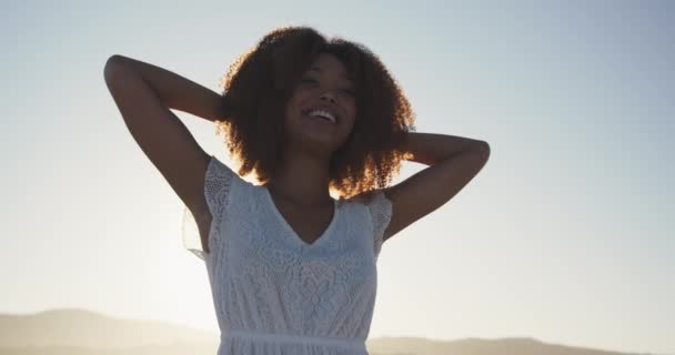 熱帯のビーチで太陽の下で時間を楽しんでいるアフリカ系アメリカ人女性のフロントビュー 離れて見て 彼女の頭の後ろに手で笑みを浮かべて レンズフレアでバックライト スローモーションで — ストック動画